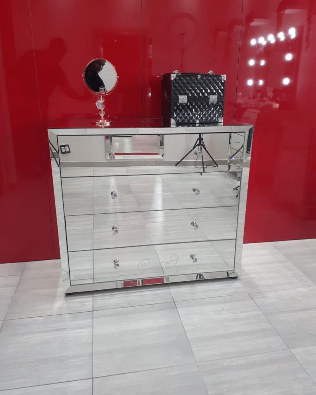 Mirrored dresser with crystal knobs against a vibrant red wall and grey tiles.