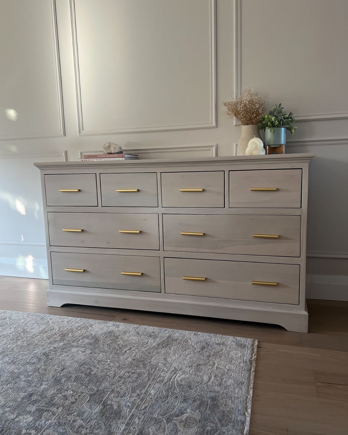 Grey painted dresser with modern gold bar handles against a paneled wall.