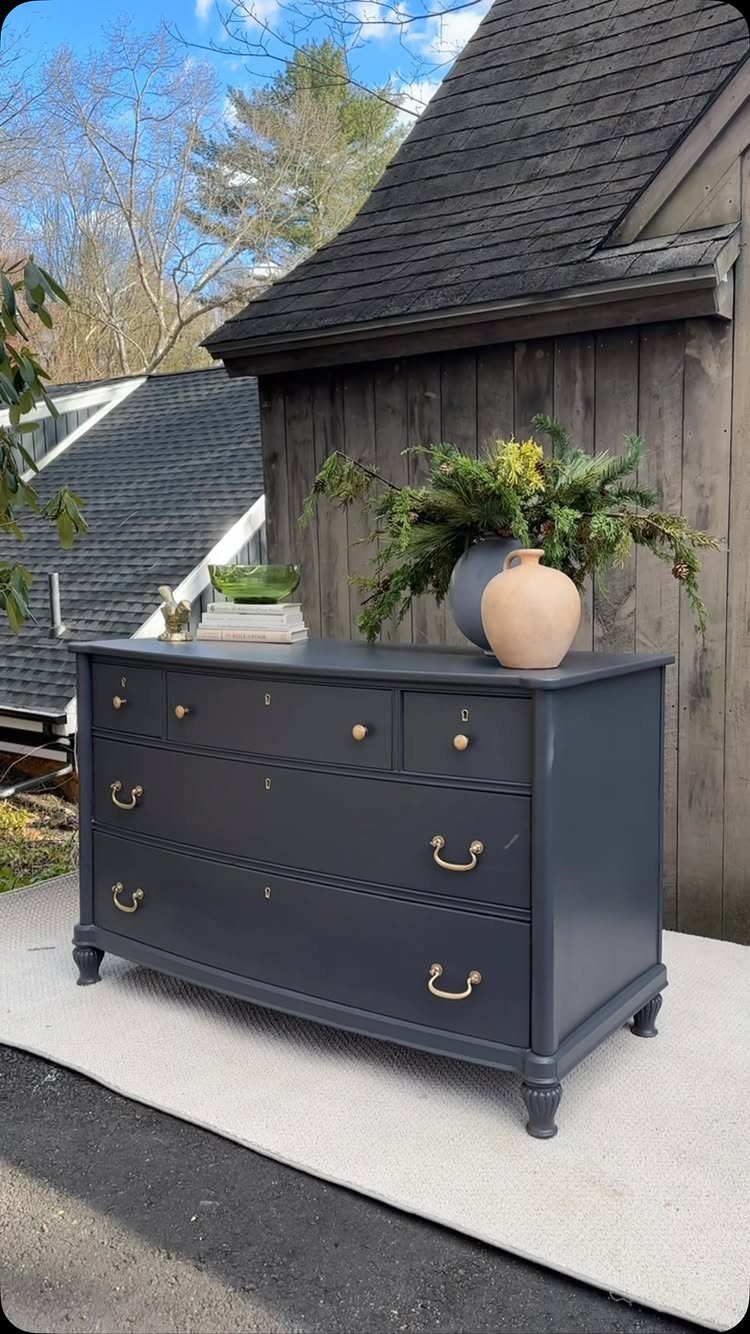 Dark grey painted dresser with gold handles and small turned legs on a rug.
