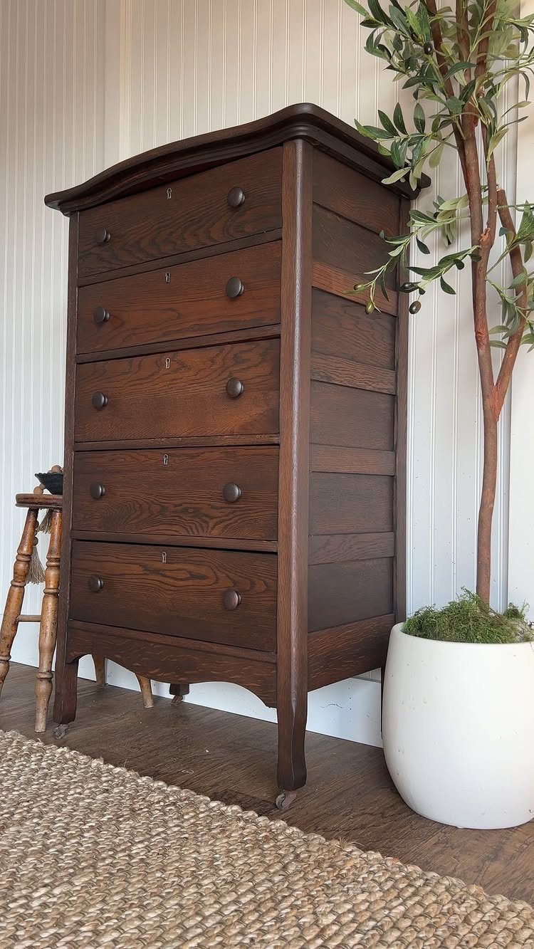 Dark brown stained wood dresser with round knobs standing next to a potted plant.