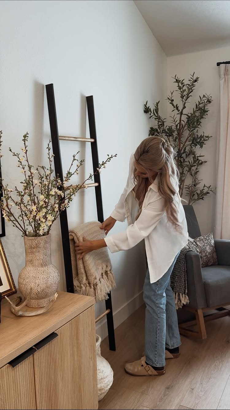 14 Easy Things to Make Out of Wood for Beginners 9 Woman placing a cream blanket on a black wooden decorative ladder against a wall.