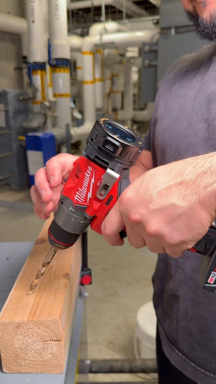Red cordless power drill boring a hole into a thick wooden beam.