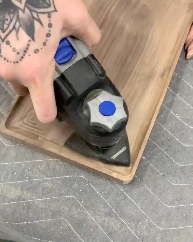 Electric hand planer smoothing the surface of a light brown wooden board.