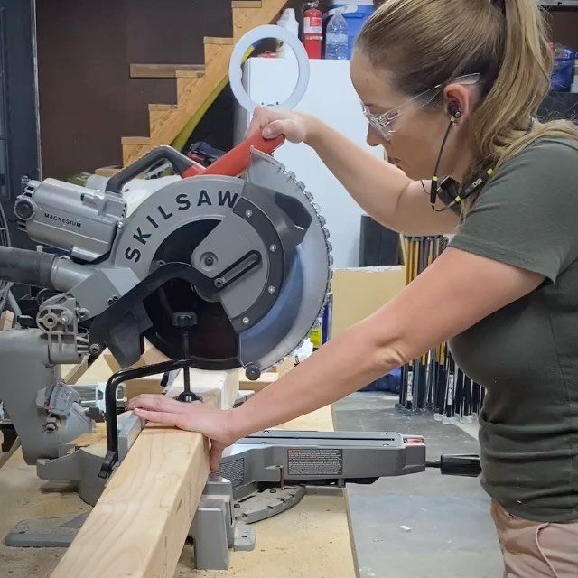 Woman using a grey electric miter saw to cut a wooden beam