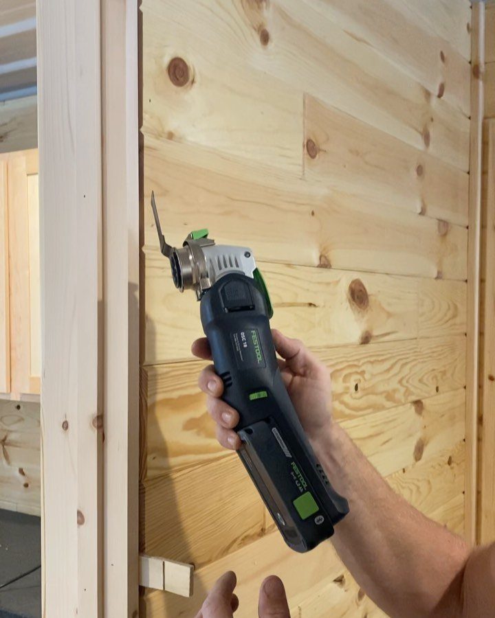 Cordless oscillating multi-tool being held against a light-colored wooden plank wall.