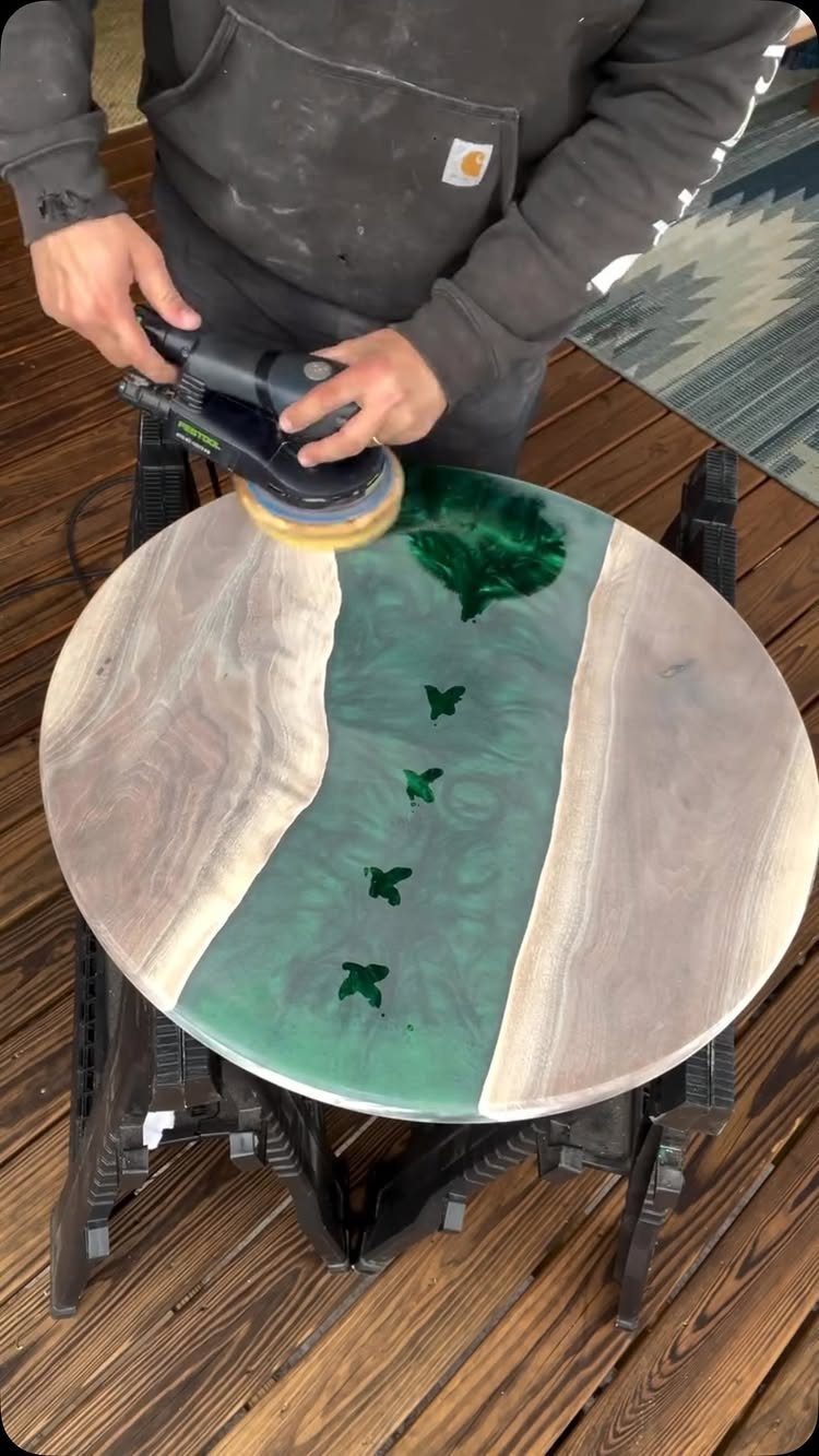 9 Epoxy Resin Wood Projects: Tables, Trays, Clocks and Coasters 1 Person sanding a round wooden table with a green epoxy resin river inlay.