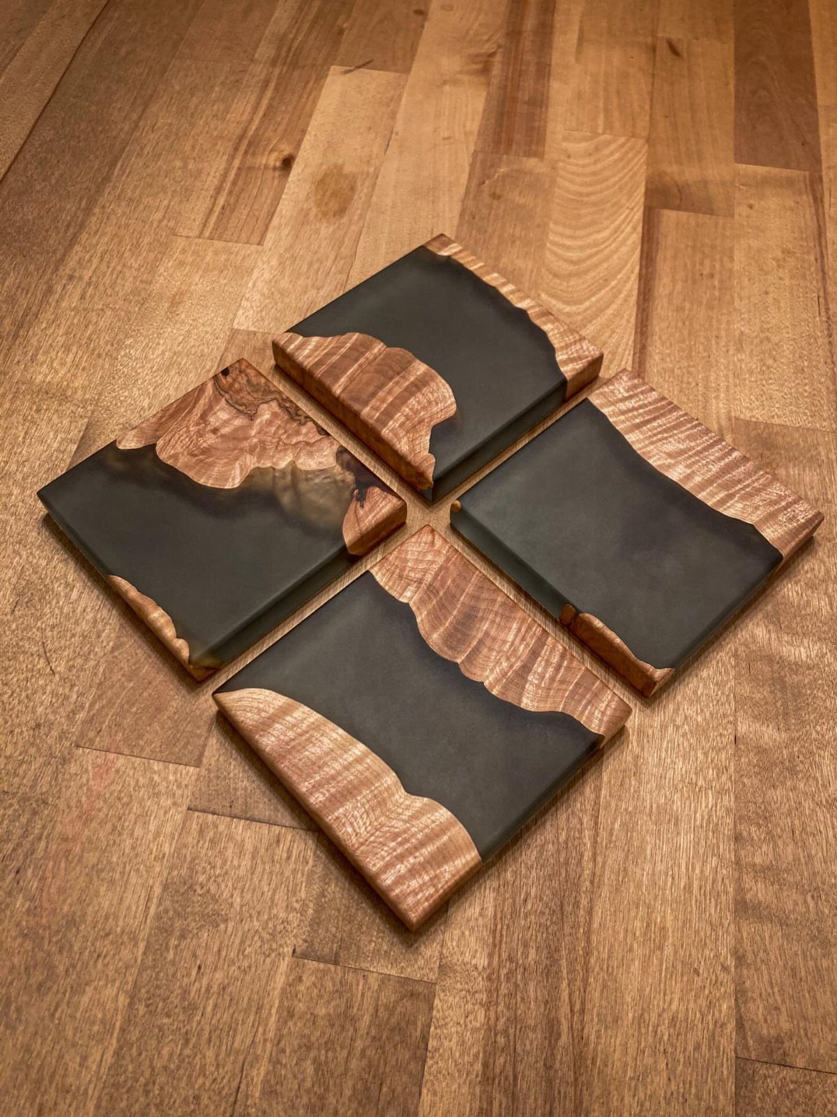 9 Epoxy Resin Wood Projects: Tables, Trays, Clocks and Coasters 5 Four wood and black epoxy resin coasters resting on a light wooden floor.