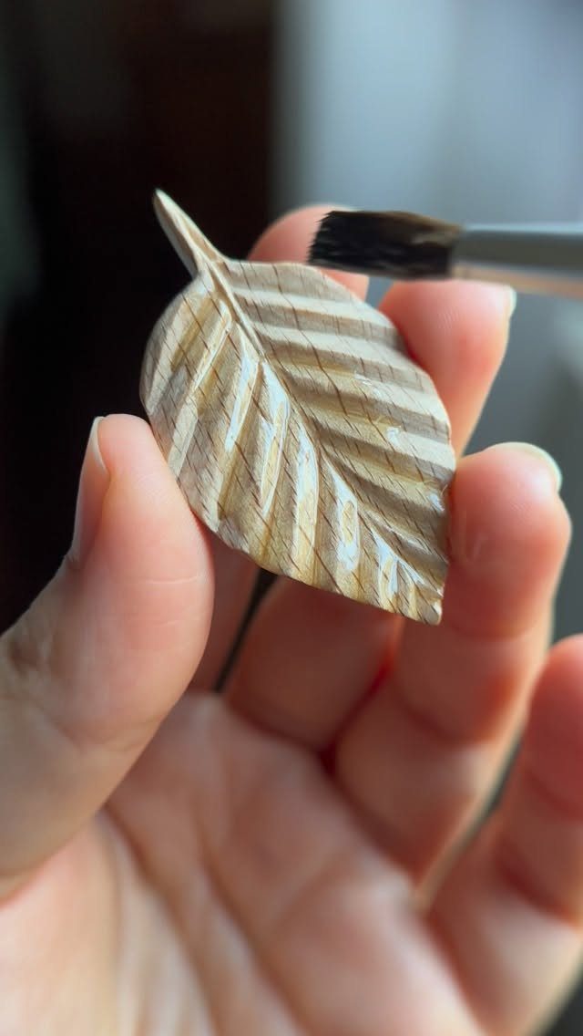 Wooden leaf carving being painted with a brush while held in a hand.