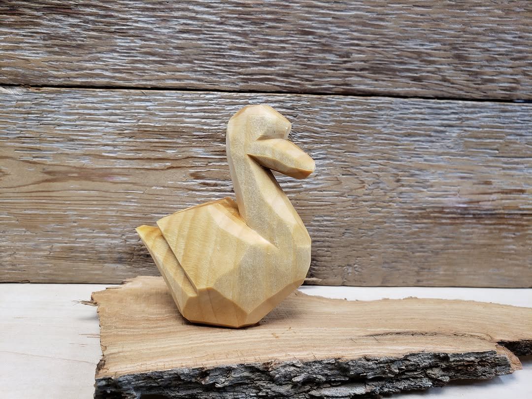 Hand-carved wooden bird with faceted cuts resting on a piece of natural bark.