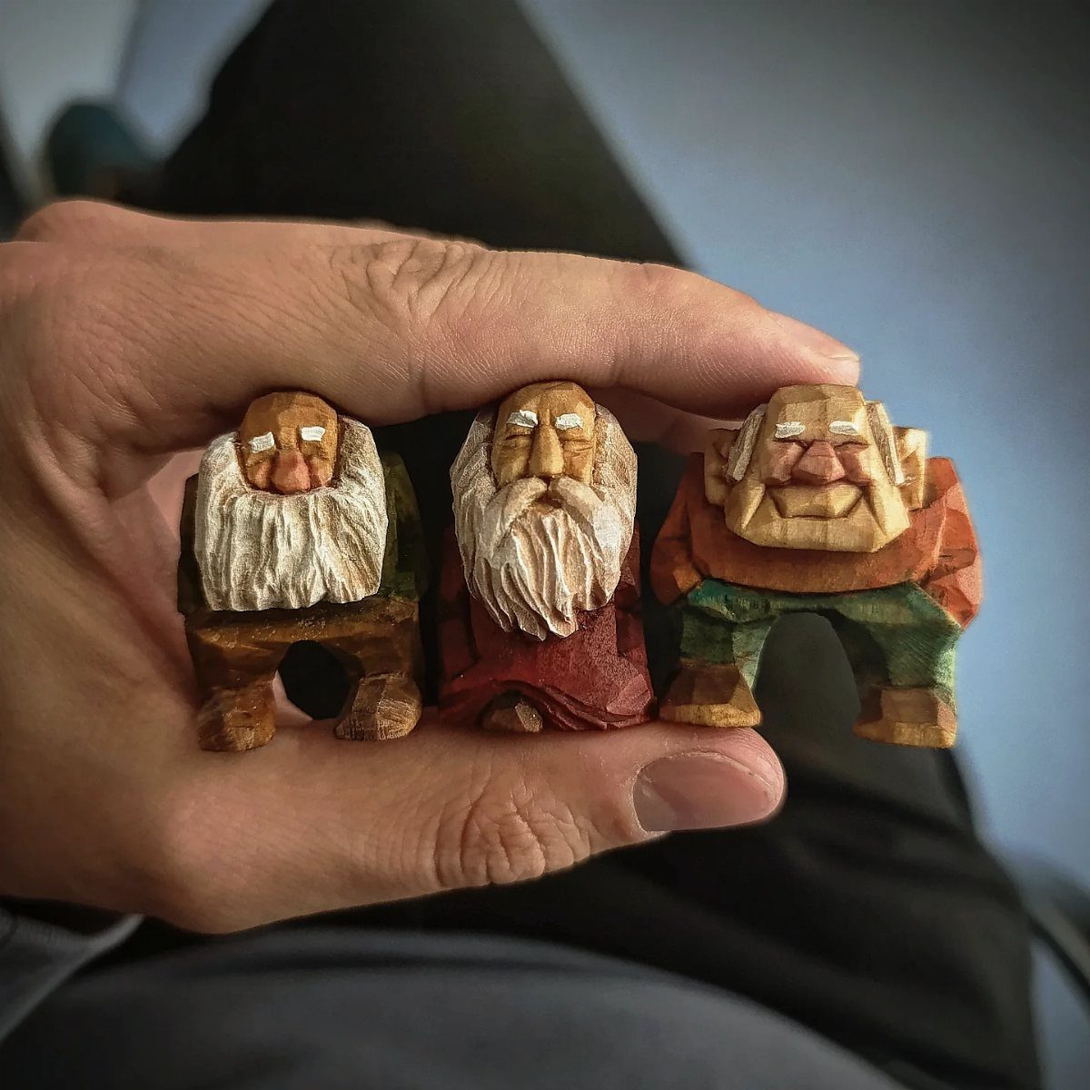 Three small hand-carved wooden gnomes with white beards held in a person's hand.