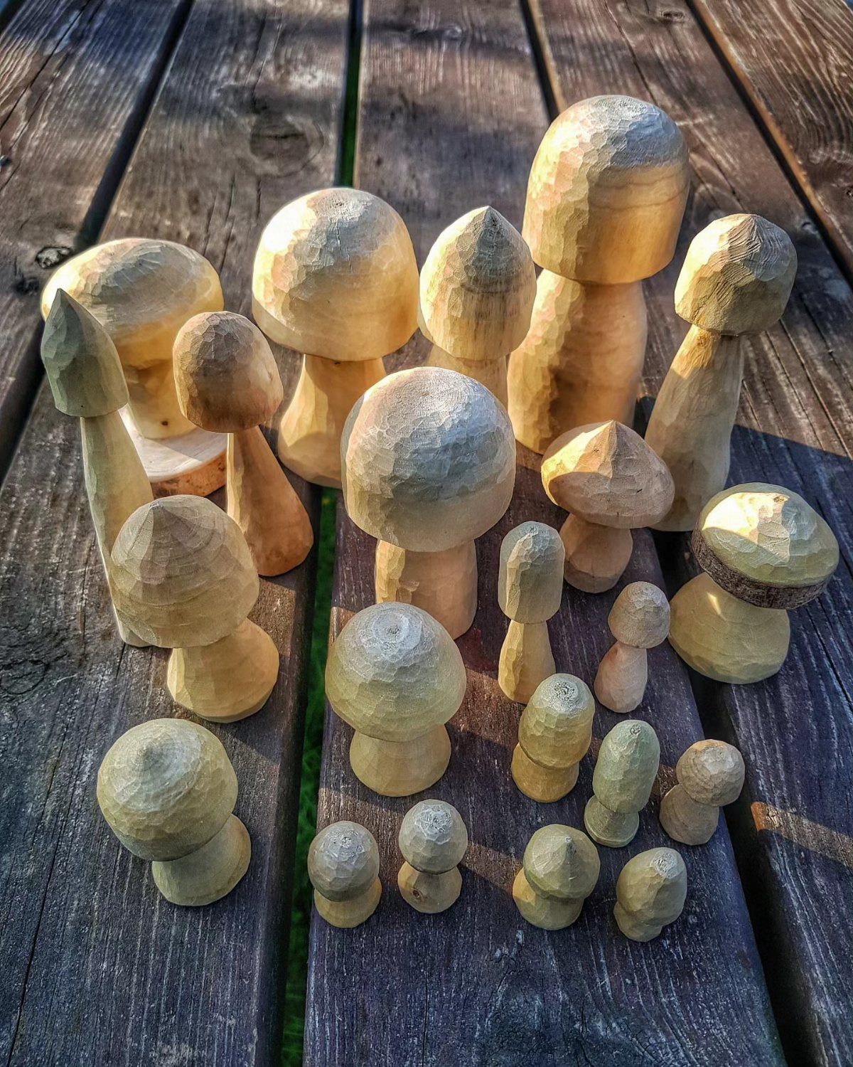 Hand-carved wooden mushrooms of various sizes resting on a weathered grey wooden deck.