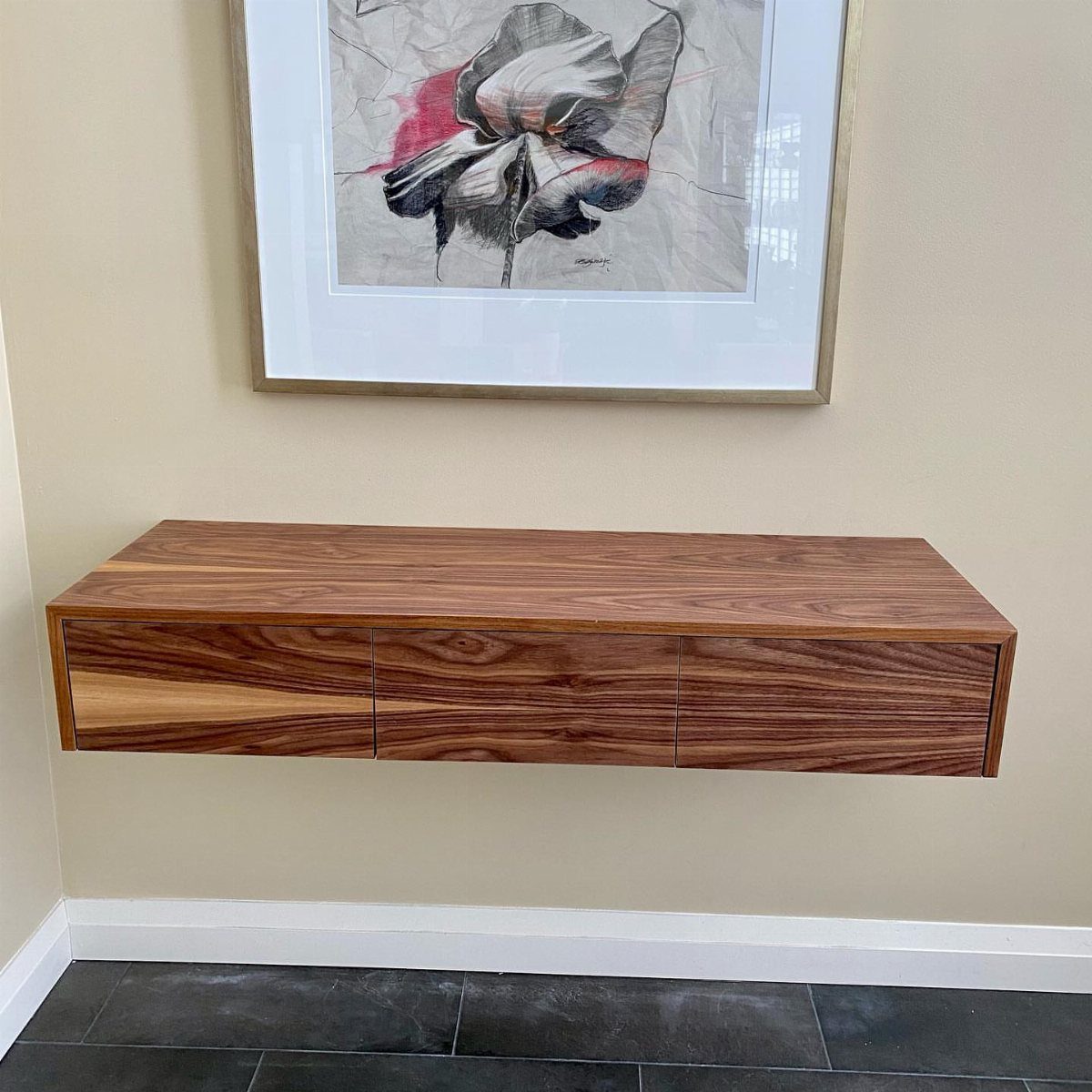 Brown wood floating shelf with drawers mounted on a beige wall below artwork