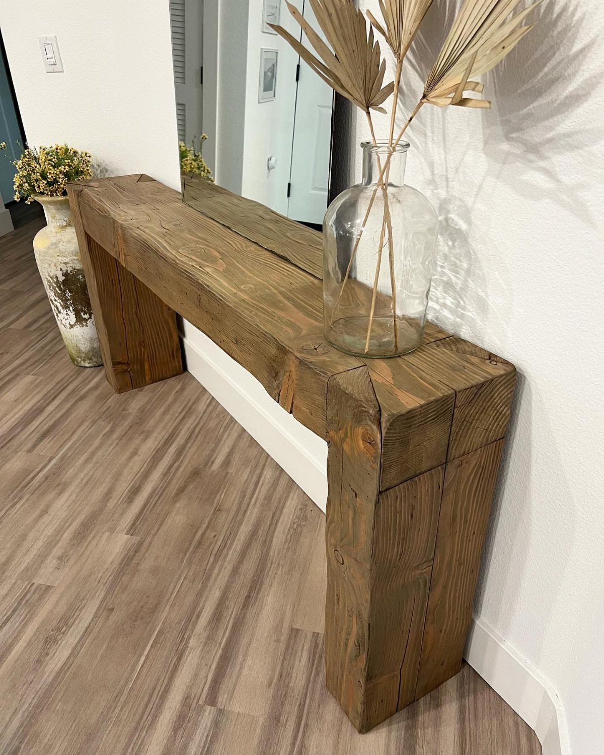 Rustic wooden bench made from reclaimed timber beams with a glass vase of leaves.
