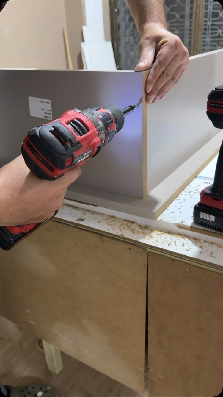 Furniture Making Tools: 11 Hand and Power Tools to Own 10 Person using a red power drill to assemble light-colored wooden furniture boards.