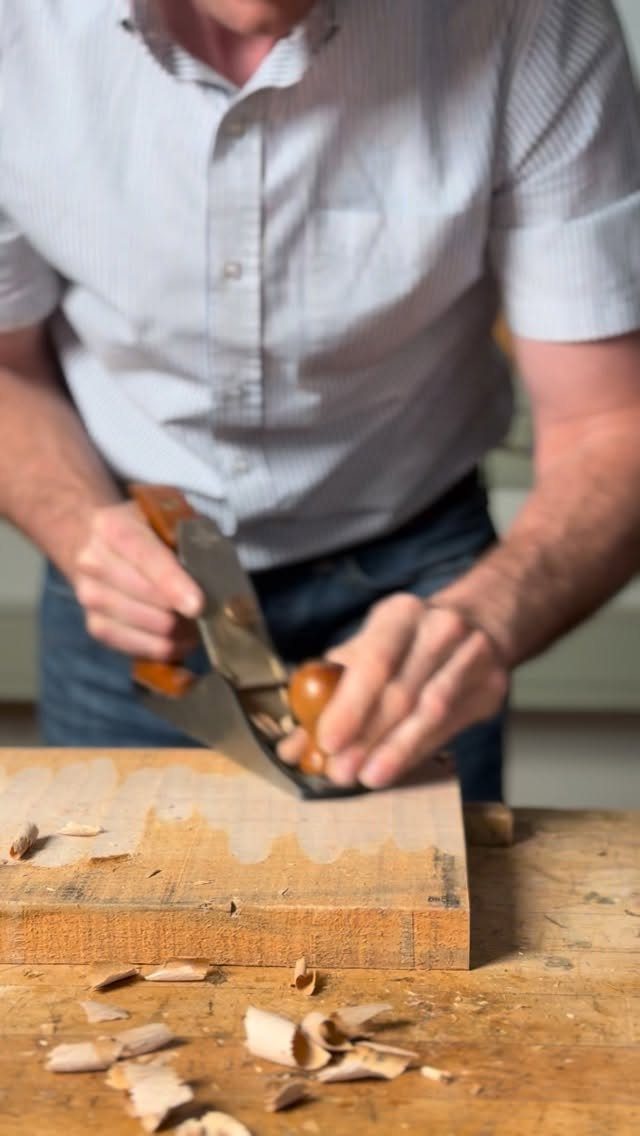 Furniture Making Tools: 11 Hand and Power Tools to Own 3 Person using a hand plane to shave a wooden block on a workbench.