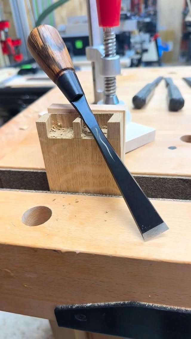 Furniture Making Tools: 11 Hand and Power Tools to Own 2 Woodworking chisel with wooden handle resting on a light-colored wooden workbench in a workshop.