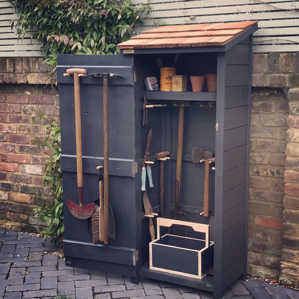 10 Garden Tool Storage Ideas for Any Yard or Garage 5 Grey wooden garden tool shed with open door showing organized hand tools inside.