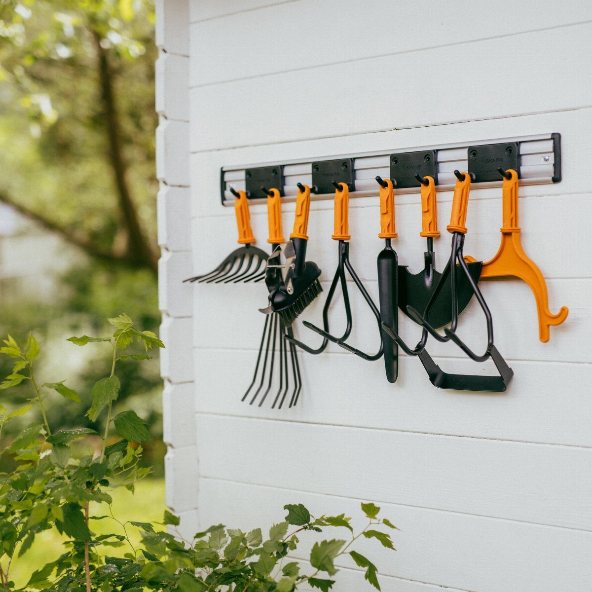 10 Garden Tool Storage Ideas for Any Yard or Garage 6 Garden tools with orange handles hanging from black hooks on a white wall.