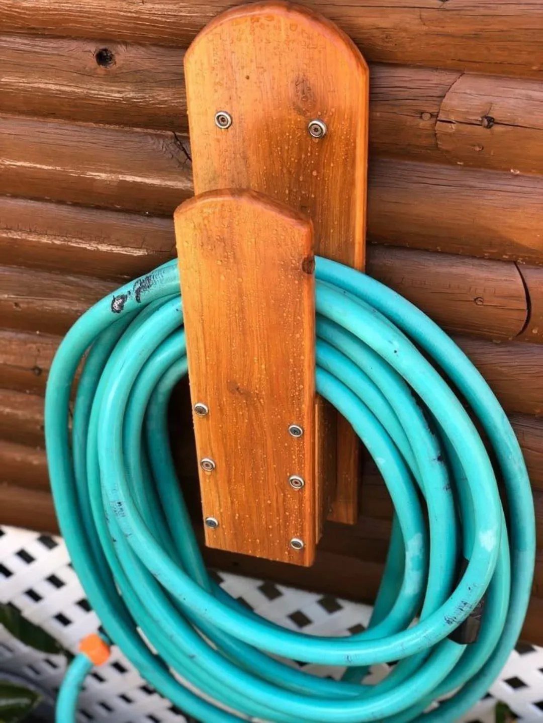 10 Garden Tool Storage Ideas for Any Yard or Garage 9 Turquoise garden hose coiled on a wooden wall-mounted holder against a log wall.