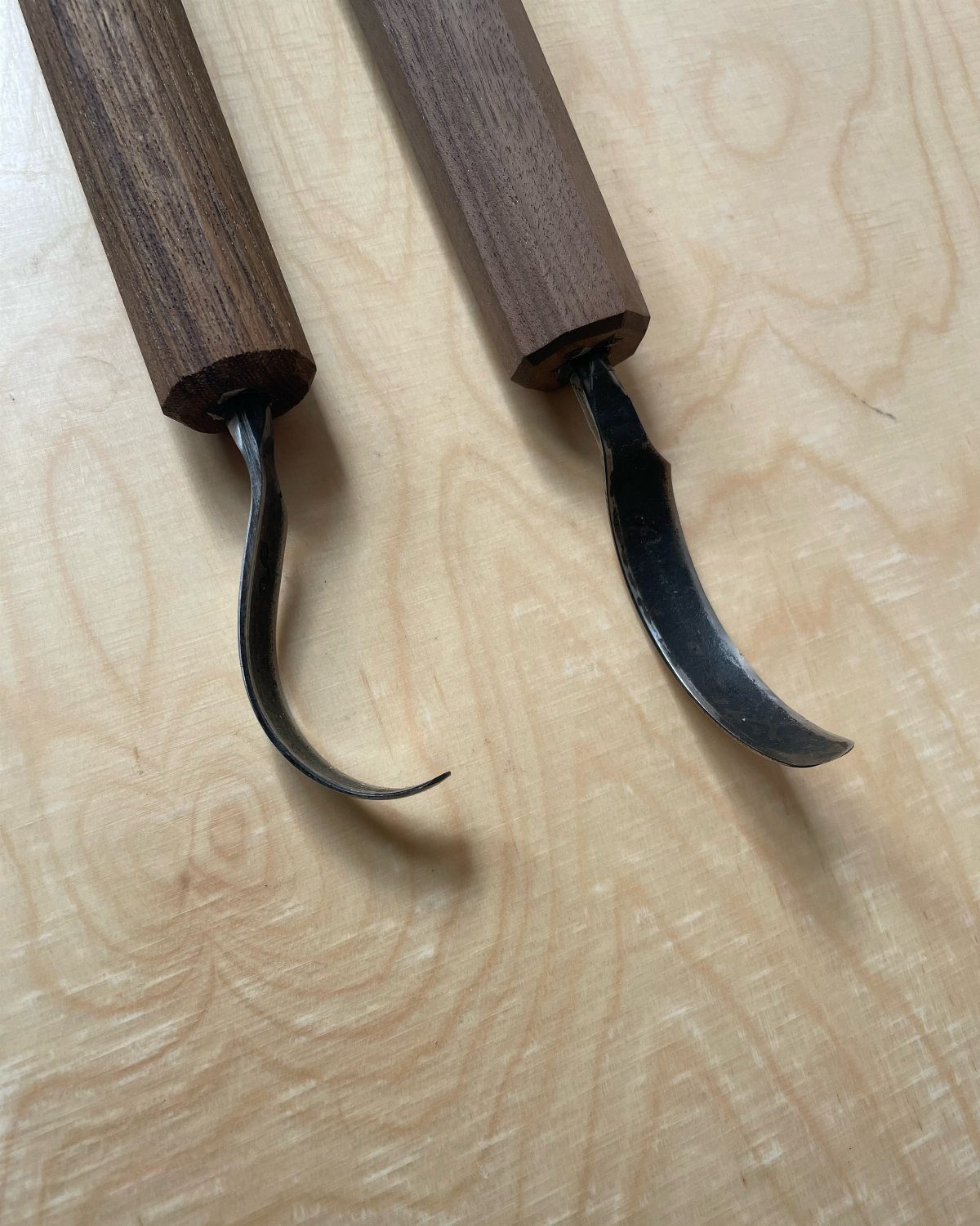 Green Woodworking Tools: 6 Essentials for the Workshop 3 Two crook knives with curved blades and wooden handles on a light wood surface.