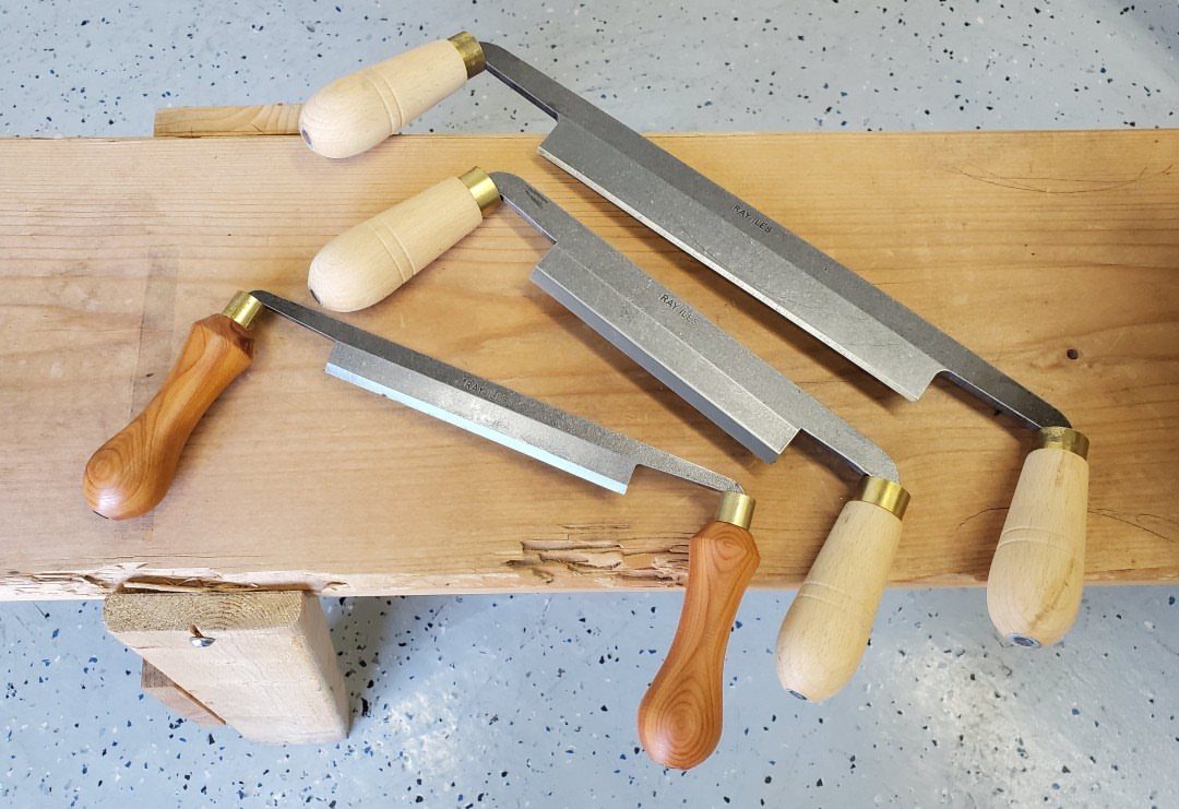 Green Woodworking Tools: 6 Essentials for the Workshop 1 Three drawknives with wooden handles resting on a thick light-colored wooden beam.