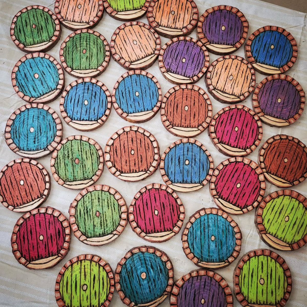 How to Burn Wood Art: 12 Ideas for Every Skill Level 2 Colorful burned wood slice art circles arranged on a white cloth background.