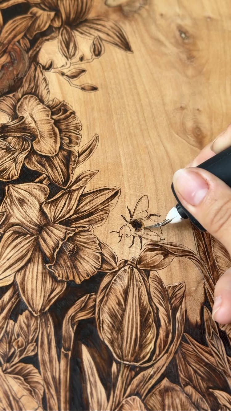 Hand using a wood burning pen to create a detailed floral design on wood.