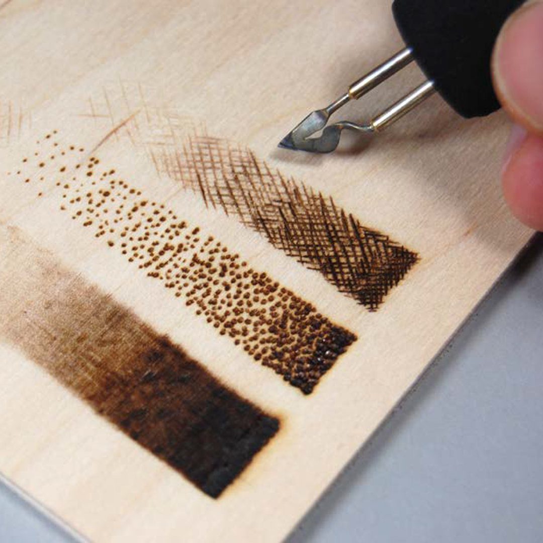 Wood burning pen tip above a wooden board showing different burned texture techniques.