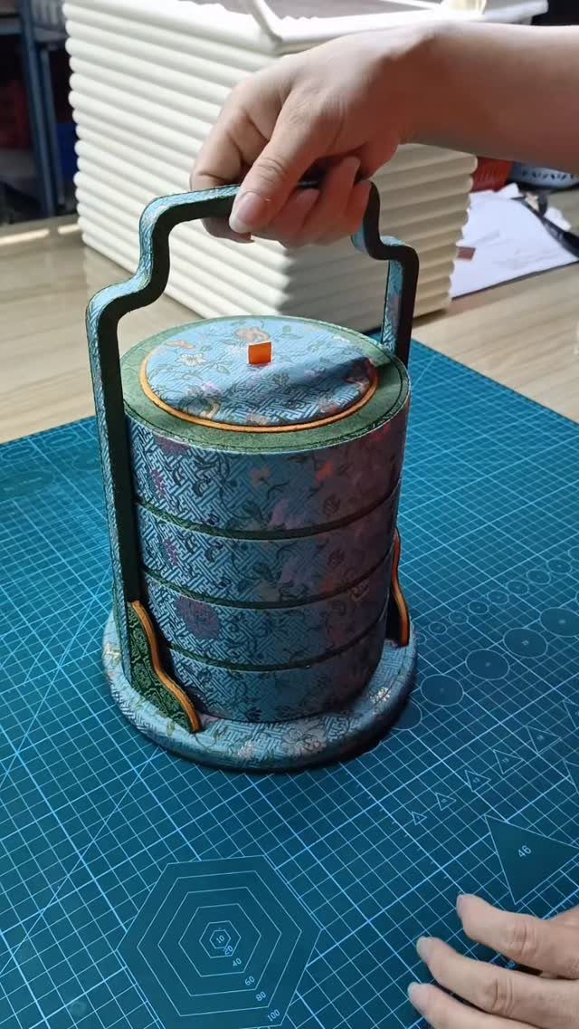 Handmade cylindrical jewelry box with blue floral fabric and a carrying handle.