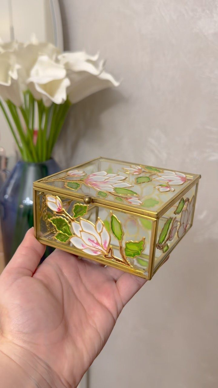 Hand-painted glass jewelry box with magnolia flowers and gold frame held in a hand.