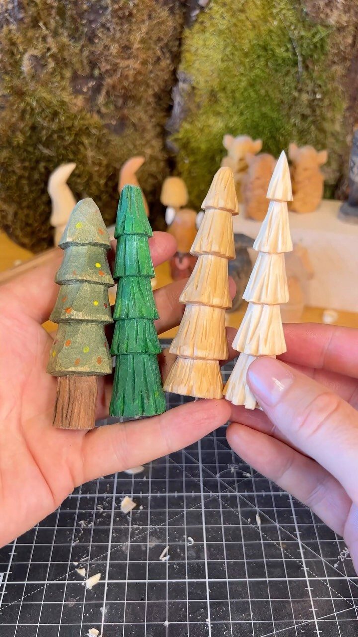 Learn How to Carve Wood: 4 Ideas to Start With 3 Four small hand-carved wooden evergreen trees held in a person's hands over a mat.