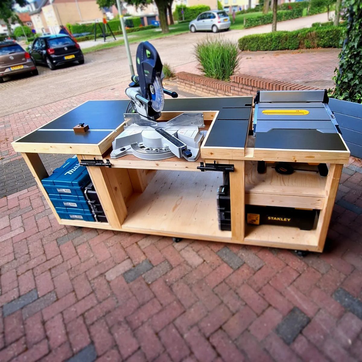 Wooden workbench with integrated miter saw and table saw and lower tool storage.