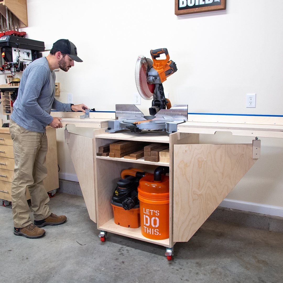Miter saw mounted on a custom plywood rolling stand with storage shelves below.