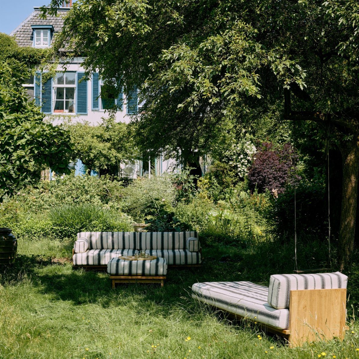 Wooden outdoor couch with striped cushions on a green lawn under leafy trees