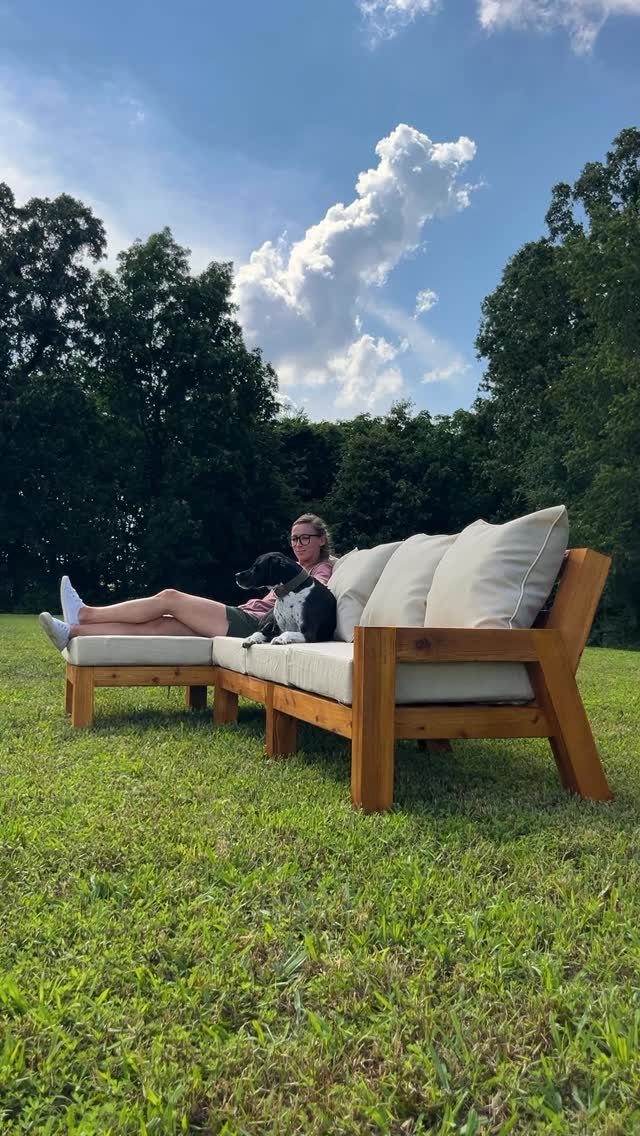 Wooden outdoor sectional sofa with cream cushions on a green lawn under a blue sky.