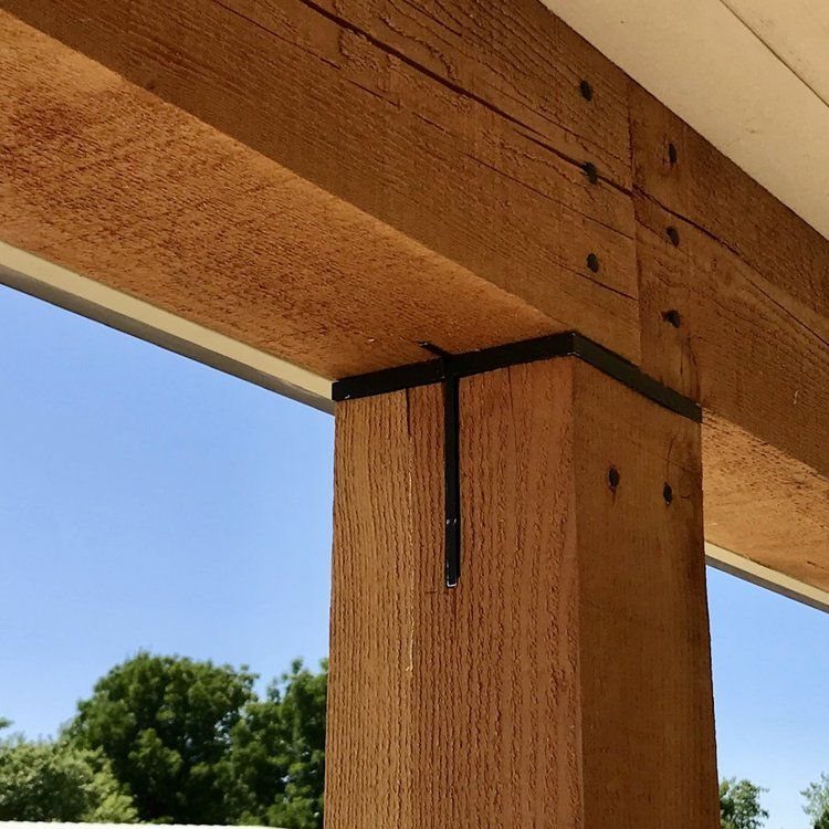 Wooden post and beam joint secured with black metal brackets under a blue sky