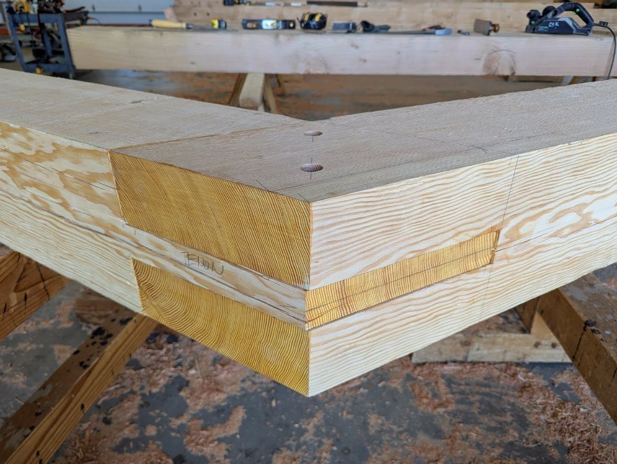 Wooden post and beam lap joint connecting two large timber beams in a workshop.