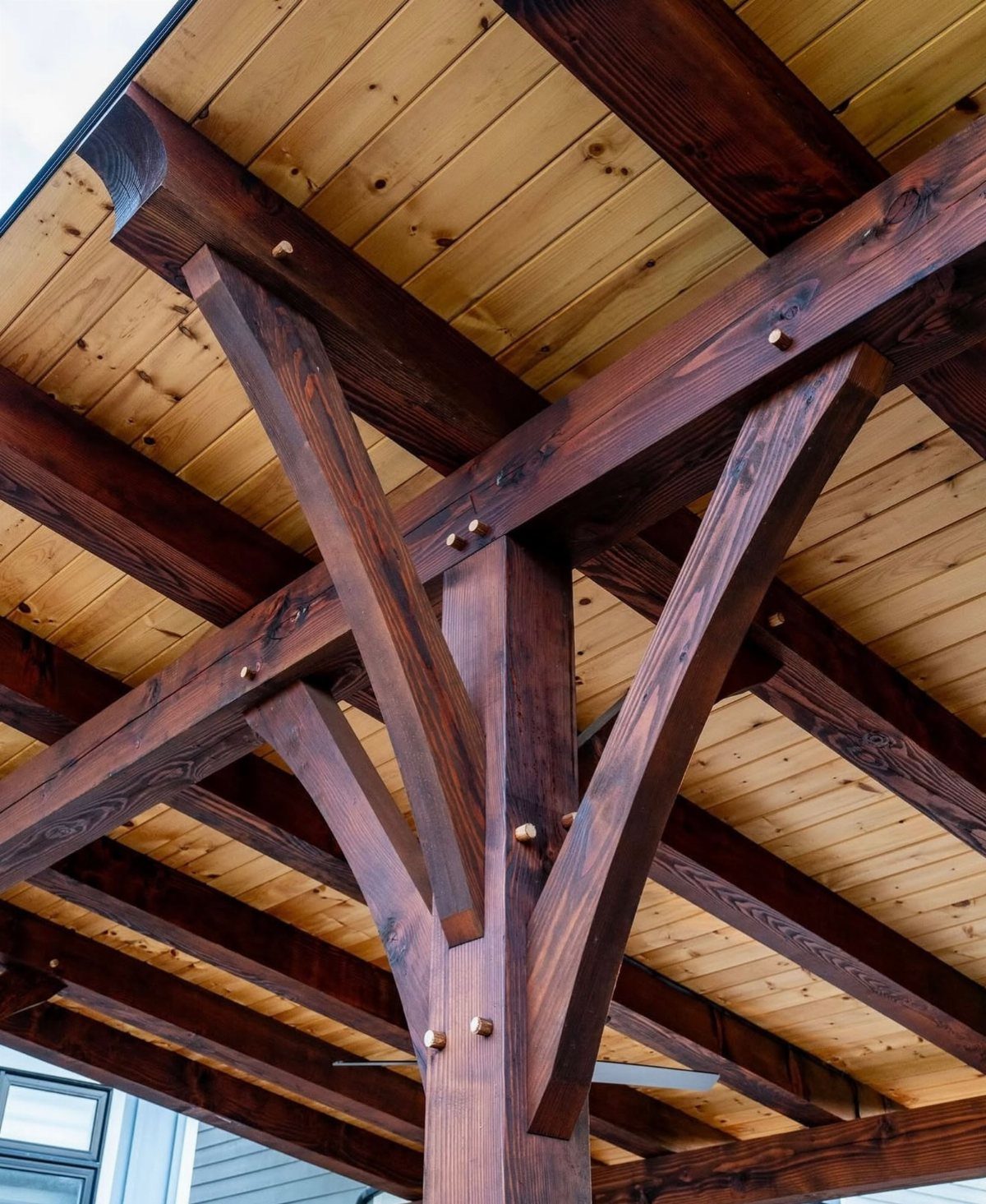 Dark brown timber post and beam structure with diagonal knee braces and wooden pegs