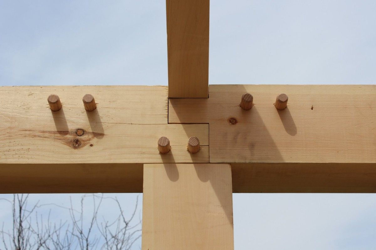 Wooden post and beam joint secured with round pegs against a clear sky.