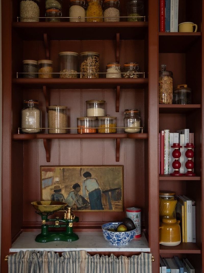 Dark wood bookcase pantry with glass jars of food and a vintage scale.