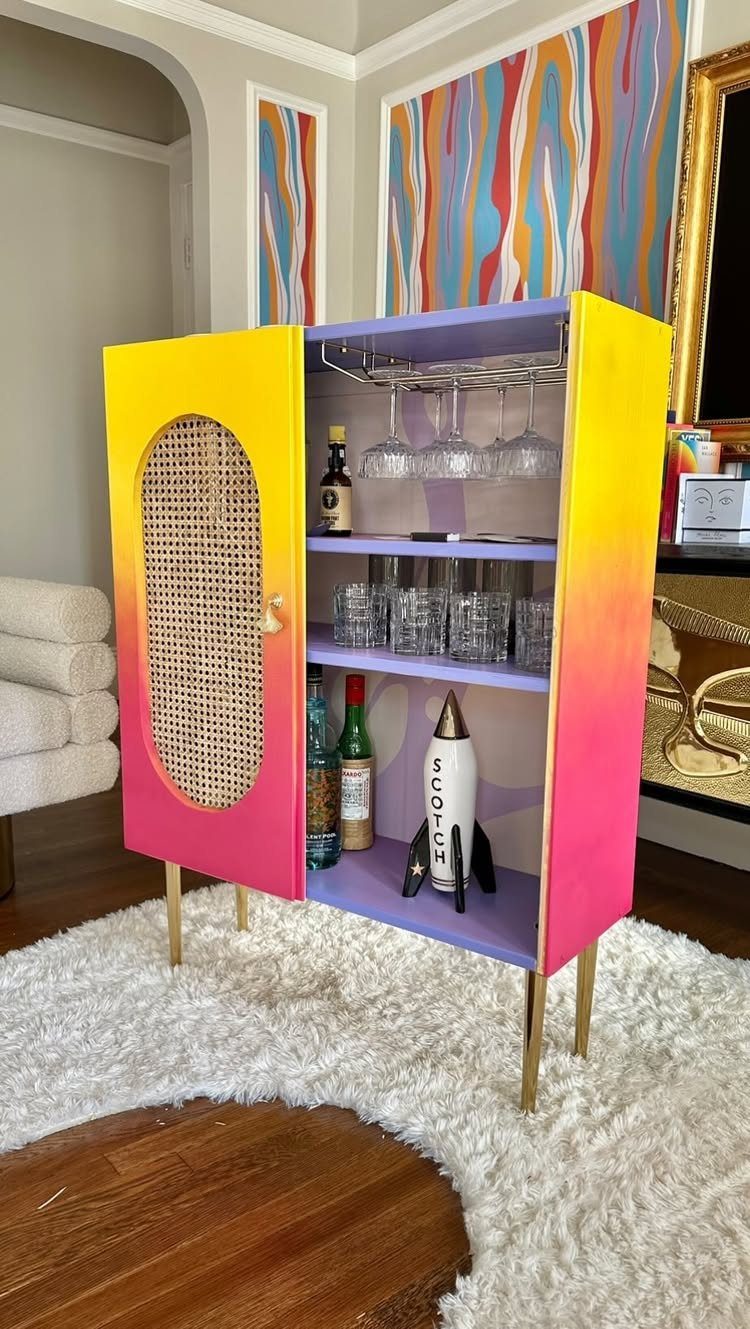 Gradient painted cabinet converted into a home bar with glassware and liquor bottles.