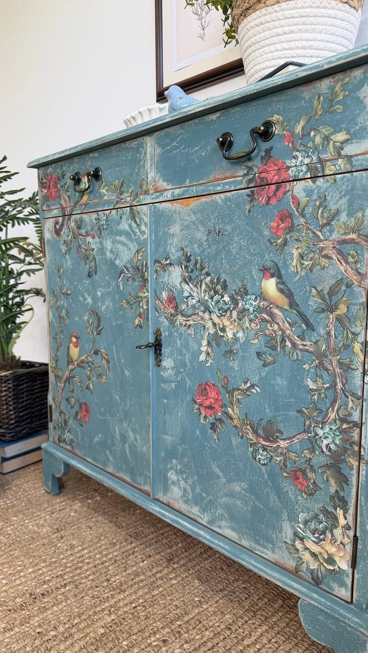 Blue distressed wooden cabinet with floral and bird paintings and dark metal hardware.