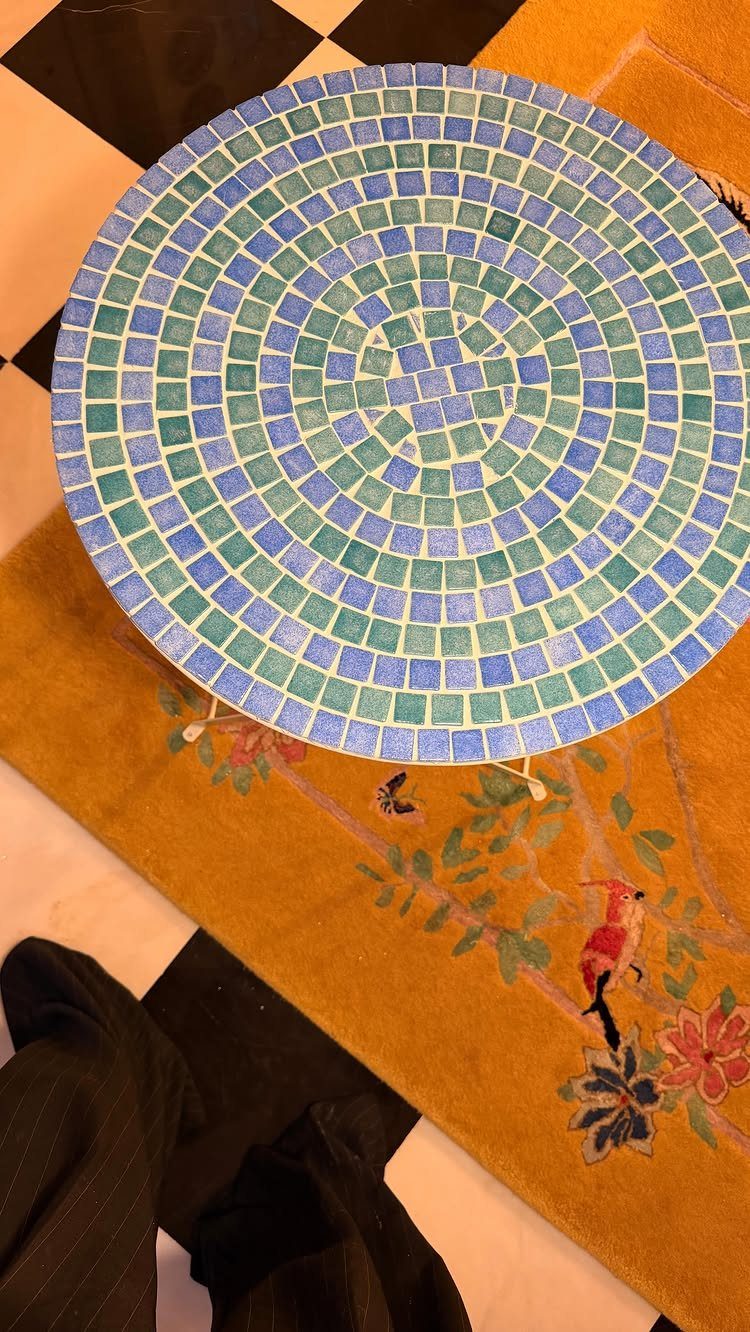 Round table with blue and green mosaic tile top on a yellow rug.