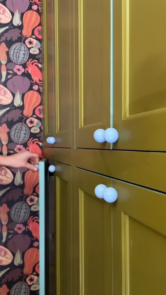 Mustard-yellow cabinet with white spherical knobs against a colorful patterned wallpaper wall.