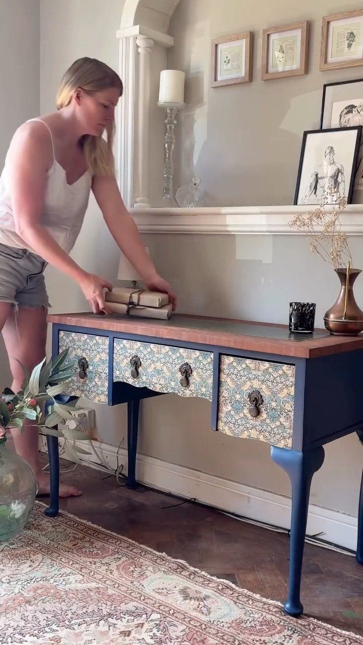 Blue painted console table with patterned drawer fronts and a woman placing books.