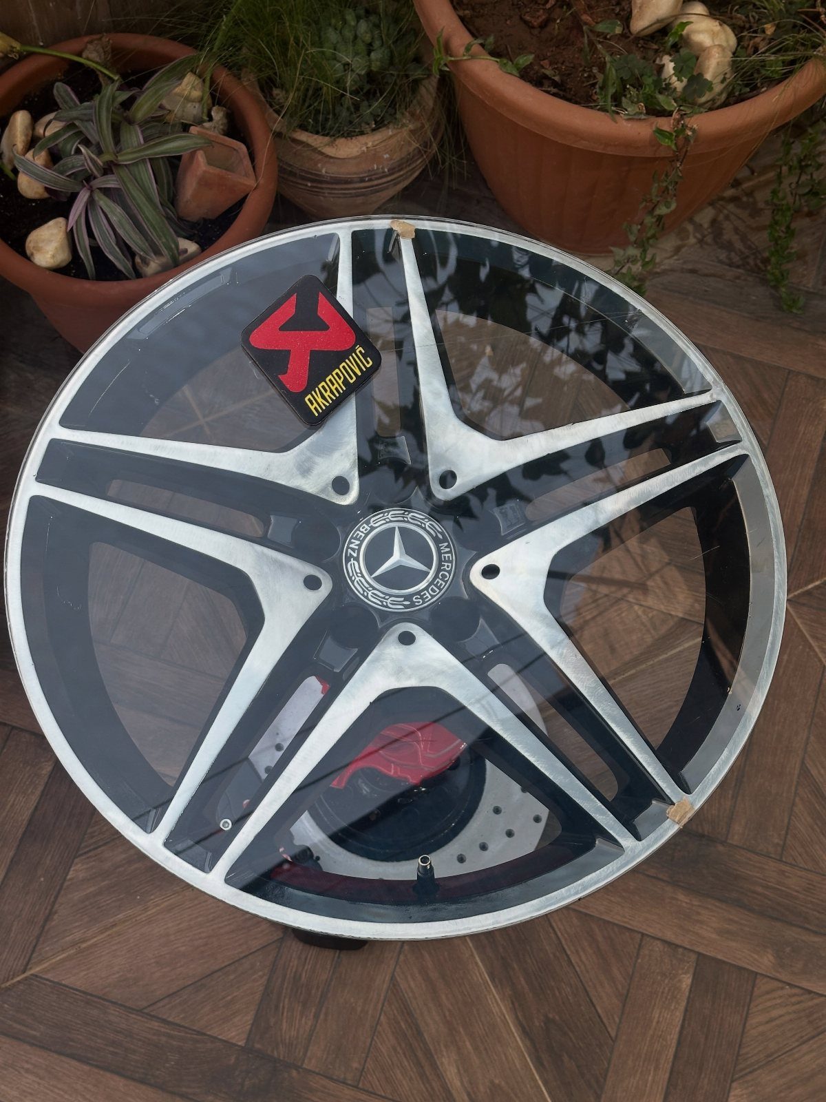 Mercedes-Benz car rim repurposed into a round glass-topped coffee table on wood flooring.