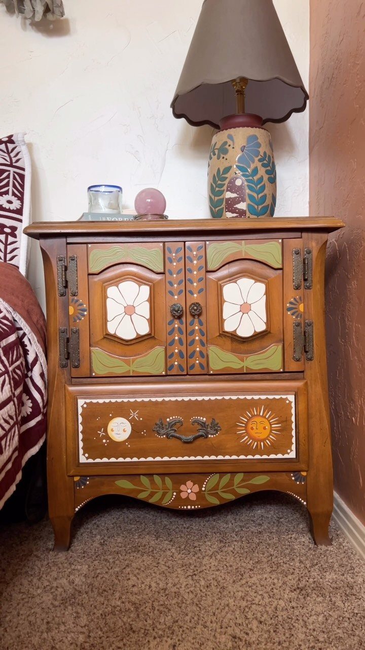 Wooden cabinet with painted floral designs and a lamp on top.