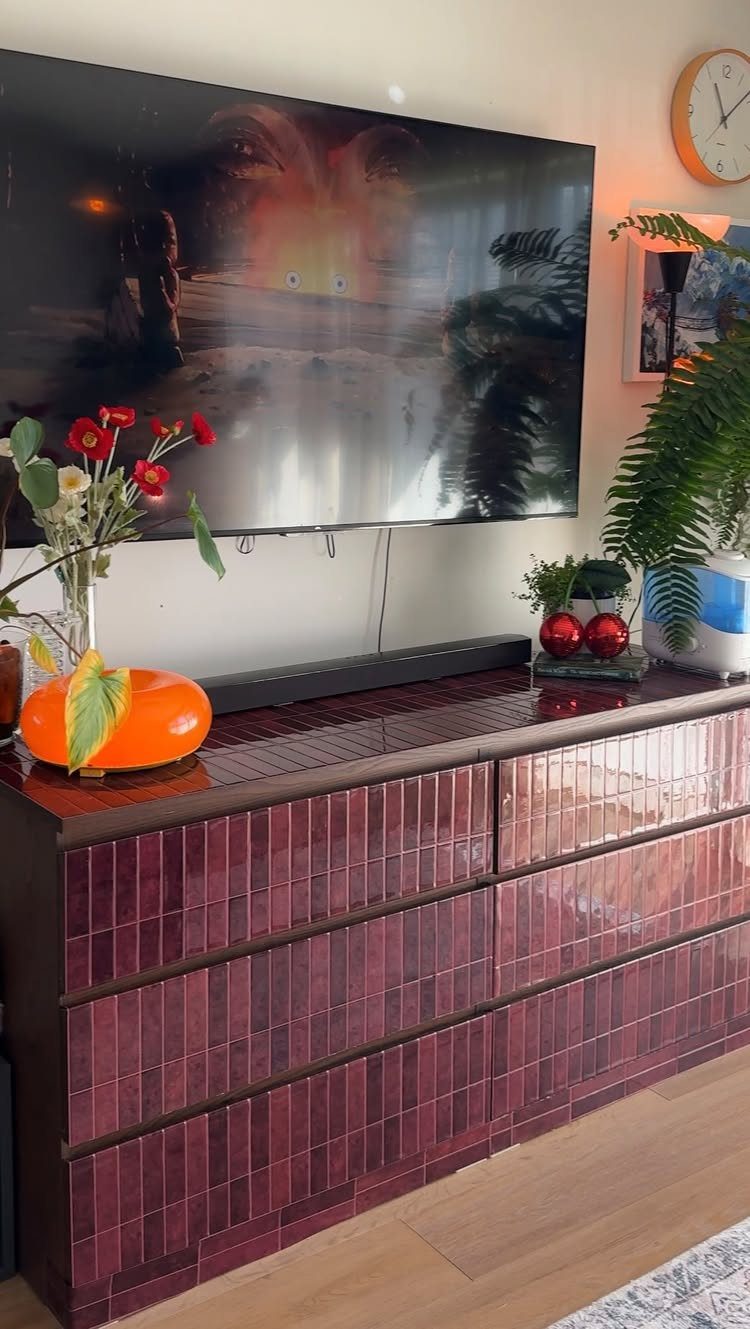 Burgundy tiled dresser under a television with red flowers and orange decor.