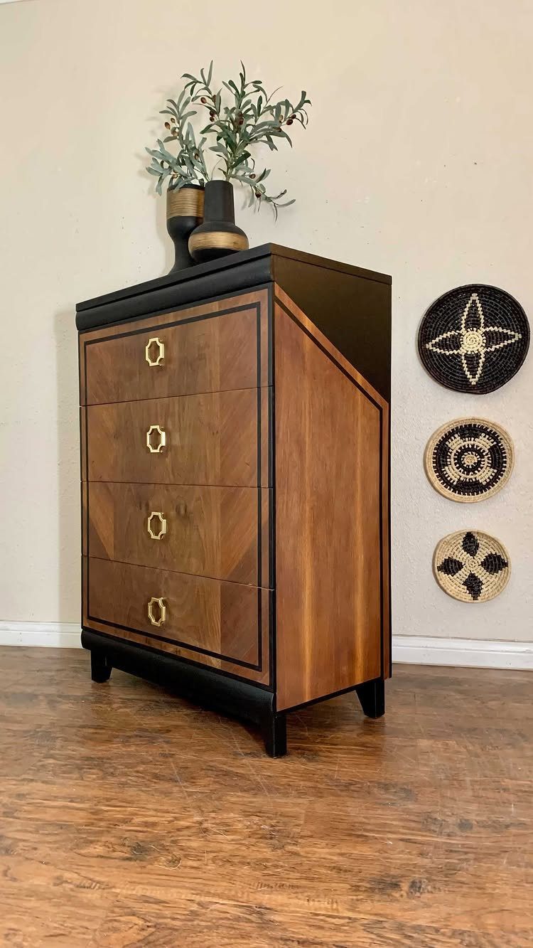 Wooden dresser with black painted trim and gold hexagonal knobs against a beige wall.
