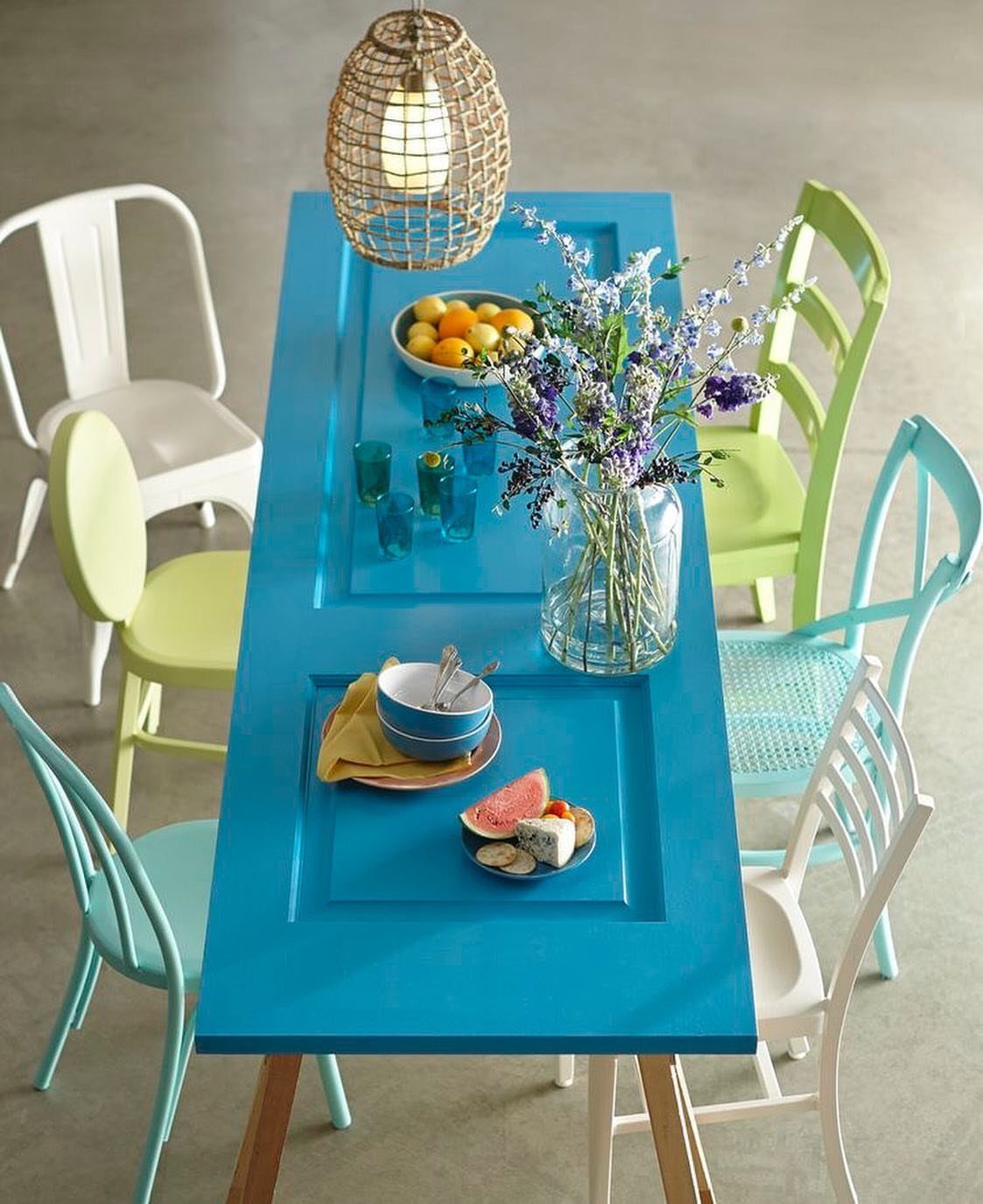 Bright blue dining table made from repurposed doors with colorful mismatched chairs.